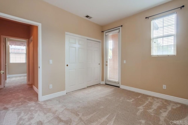 unfurnished bedroom with multiple windows, light carpet, and a closet