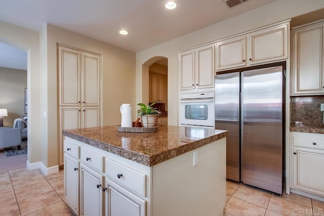 kitchen featuring stainless steel refrigerator, a center island, white oven, and dark stone countertops