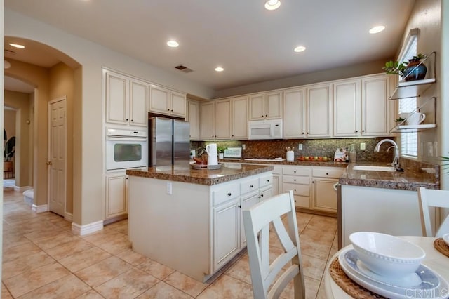 kitchen with a kitchen island, sink, light tile patterned floors, and white appliances