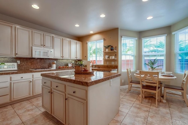 kitchen featuring tasteful backsplash, light tile patterned flooring, a kitchen island, and dark stone countertops