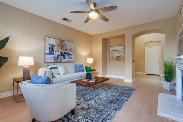 living room featuring light hardwood / wood-style flooring, a tile fireplace, and ceiling fan