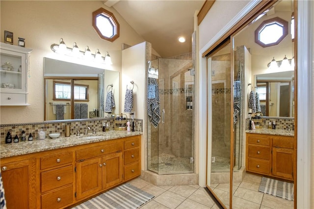 bathroom with tile patterned flooring, backsplash, vanity, vaulted ceiling, and a shower with shower door