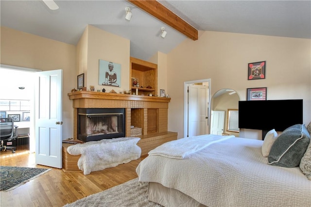 bedroom featuring hardwood / wood-style floors, a fireplace, lofted ceiling with beams, and ceiling fan