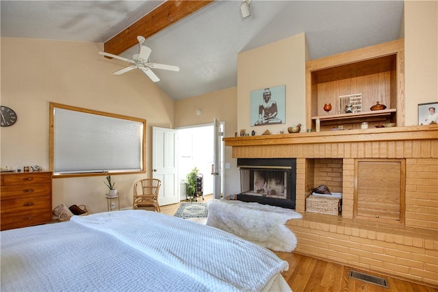 bedroom featuring vaulted ceiling with beams, a fireplace, hardwood / wood-style floors, and ceiling fan