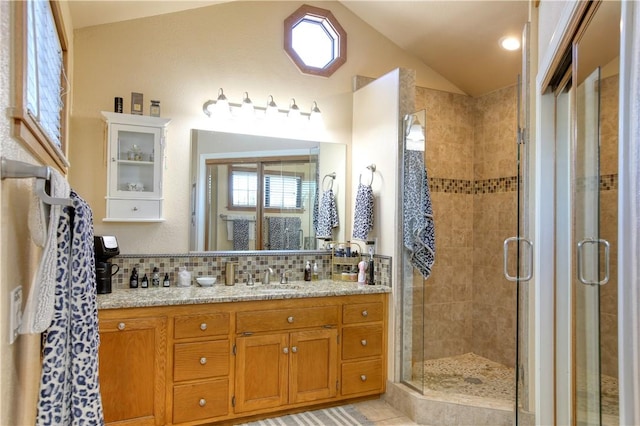 bathroom with vanity, backsplash, vaulted ceiling, and walk in shower