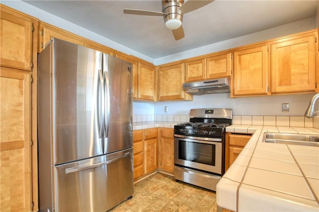 kitchen with appliances with stainless steel finishes, sink, tile counters, and ceiling fan