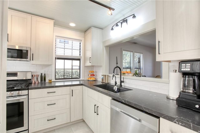 kitchen with sink, light tile patterned floors, appliances with stainless steel finishes, tasteful backsplash, and track lighting