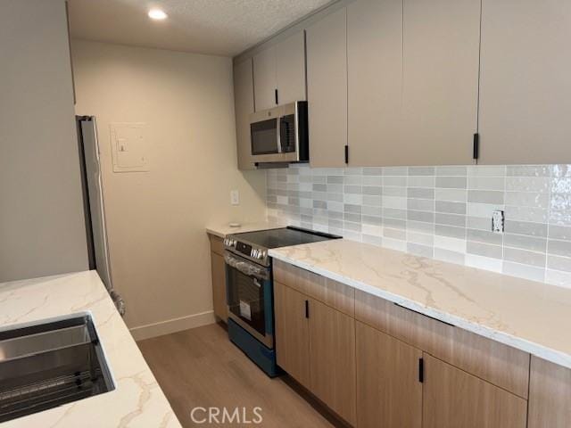 2501 W Sunflower Unit F12, Santa Ana, CA 92704 - kitchen featuring stainless steel appliances, light wood-style flooring, light stone counters, decorative backsplash, and recessed lighting