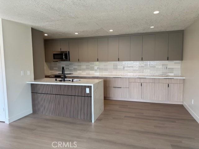 2501 W Sunflower Unit F12, Santa Ana, CA 92704 - kitchen with stainless steel microwave, decorative backsplash, wood finished floors, light countertops, and recessed lighting