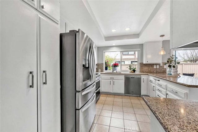 kitchen featuring appliances with stainless steel finishes, white cabinetry, a tray ceiling, decorative light fixtures, and dark stone counters