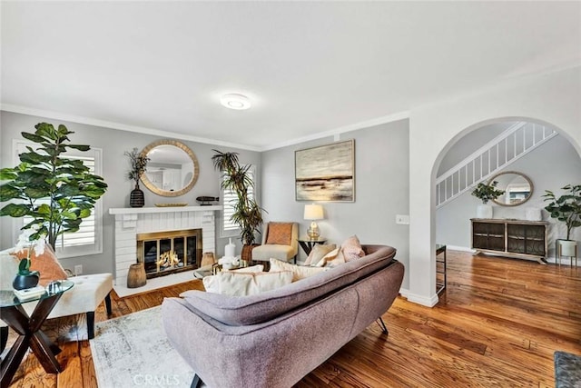 living room with a brick fireplace, hardwood / wood-style flooring, and ornamental molding