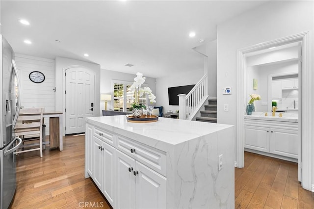 kitchen featuring light stone counters, stainless steel fridge, a kitchen island, light hardwood / wood-style floors, and white cabinets