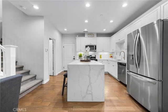 kitchen featuring appliances with stainless steel finishes, white cabinetry, a breakfast bar area, a center island, and light hardwood / wood-style flooring