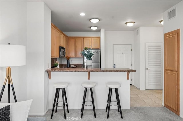 kitchen with stainless steel refrigerator, dark stone countertops, a breakfast bar area, light tile patterned floors, and kitchen peninsula