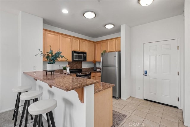 kitchen with stainless steel appliances, kitchen peninsula, dark stone counters, and a breakfast bar