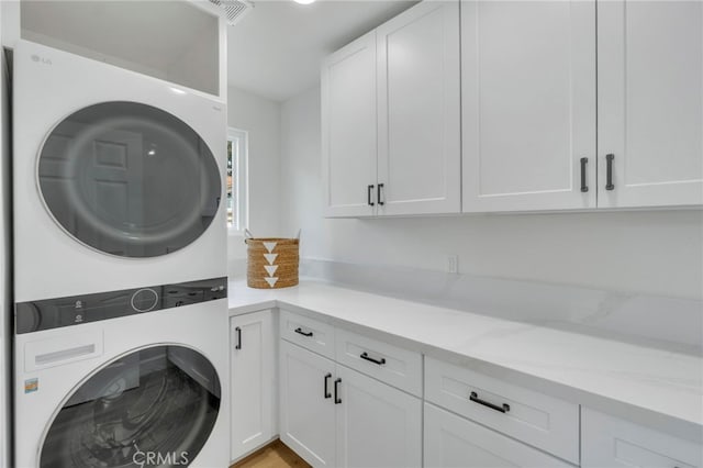 laundry room featuring stacked washer / drying machine and cabinets