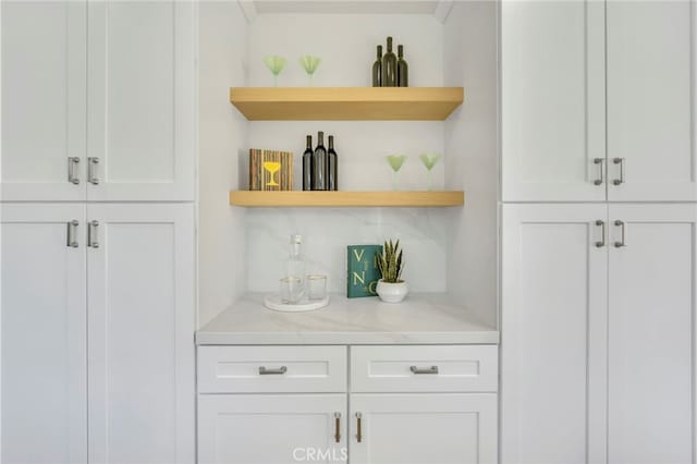 bar featuring light stone counters and white cabinets