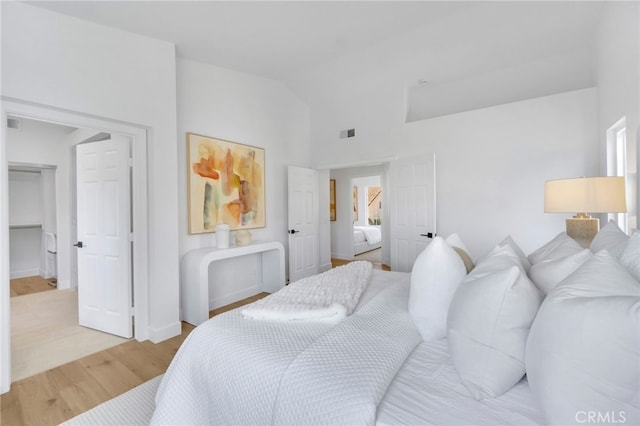 bedroom with wood-type flooring, a walk in closet, lofted ceiling, and a closet