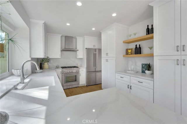 kitchen with light stone counters, sink, wall chimney exhaust hood, and high quality appliances