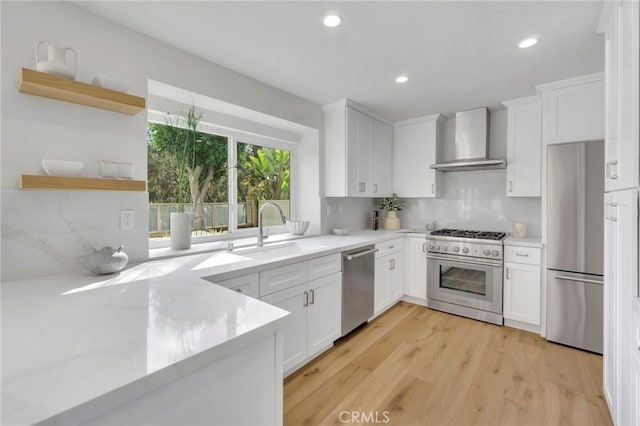 kitchen featuring white cabinetry, stainless steel appliances, and wall chimney range hood