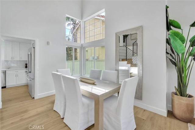 dining room featuring plenty of natural light, a towering ceiling, and light wood-type flooring