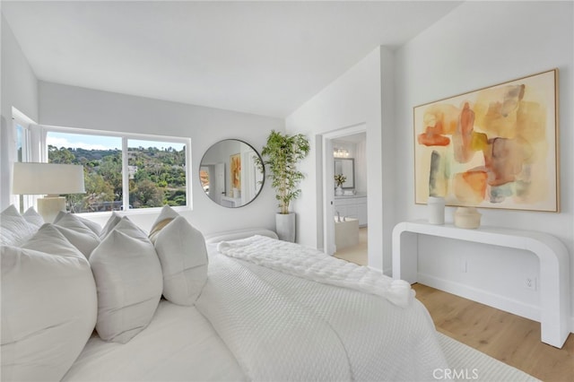 bedroom featuring hardwood / wood-style floors, ensuite bath, and vaulted ceiling