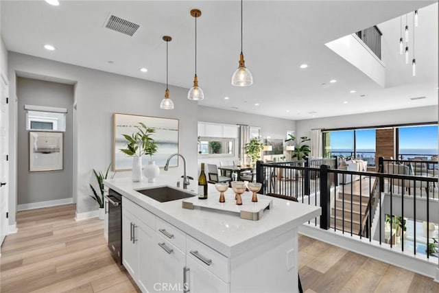 kitchen with pendant lighting, an island with sink, sink, white cabinets, and light hardwood / wood-style flooring