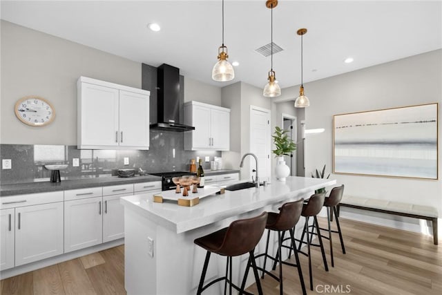 kitchen with white cabinetry, wall chimney exhaust hood, sink, and an island with sink