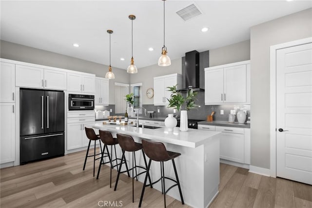 kitchen featuring sink, high quality fridge, white cabinets, decorative light fixtures, and wall chimney exhaust hood