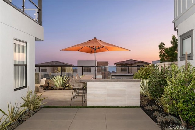 patio terrace at dusk featuring exterior kitchen and an outdoor bar