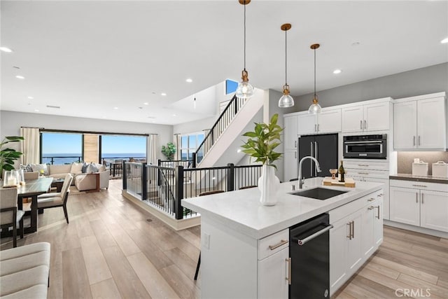 kitchen with sink, black appliances, pendant lighting, a kitchen island with sink, and white cabinets