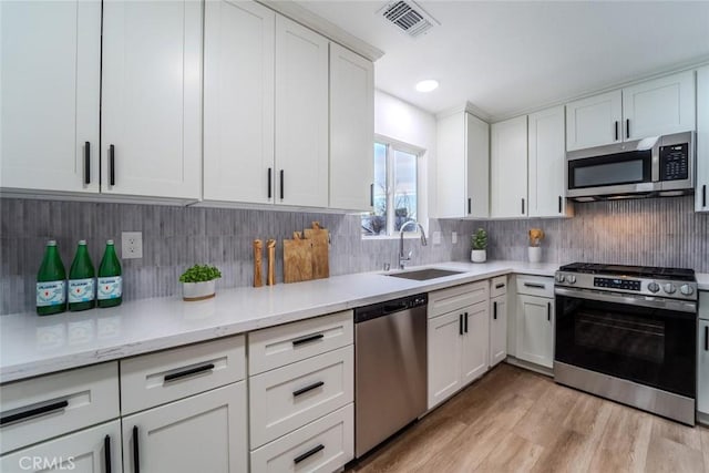 kitchen with appliances with stainless steel finishes, sink, white cabinets, and light hardwood / wood-style floors