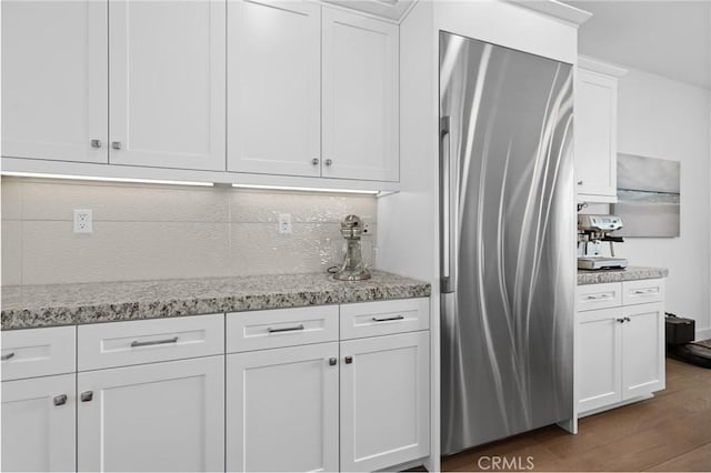 kitchen with dark wood-type flooring, white cabinetry, light stone counters, stainless steel refrigerator, and decorative backsplash