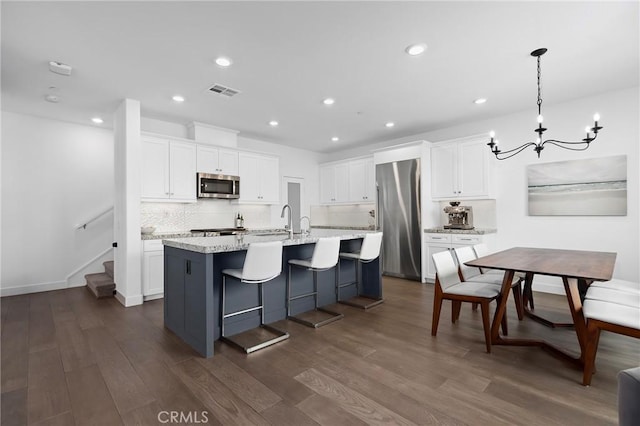 kitchen featuring pendant lighting, stainless steel appliances, white cabinets, a center island with sink, and dark hardwood / wood-style flooring