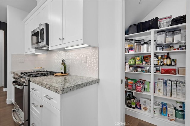 kitchen featuring appliances with stainless steel finishes, dark hardwood / wood-style flooring, white cabinets, light stone countertops, and backsplash