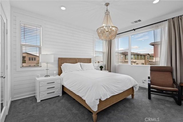 bedroom featuring an inviting chandelier, wooden walls, and dark colored carpet