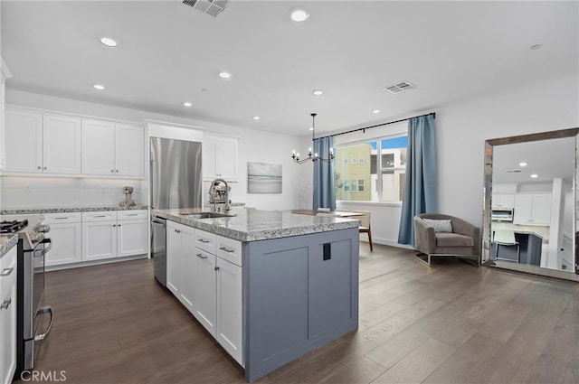 kitchen with appliances with stainless steel finishes, sink, white cabinets, light stone counters, and a center island with sink