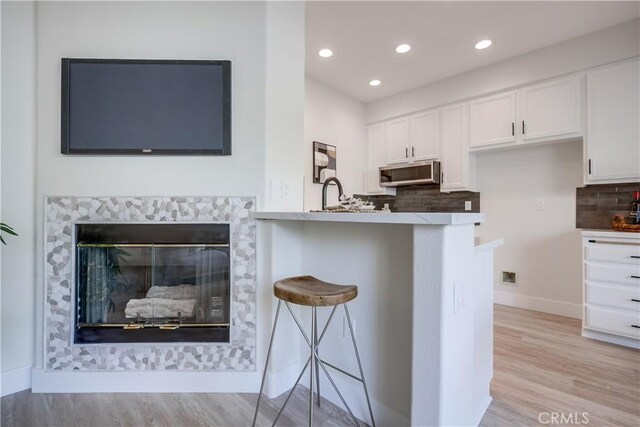 kitchen with a tile fireplace, tasteful backsplash, a breakfast bar area, white cabinets, and kitchen peninsula