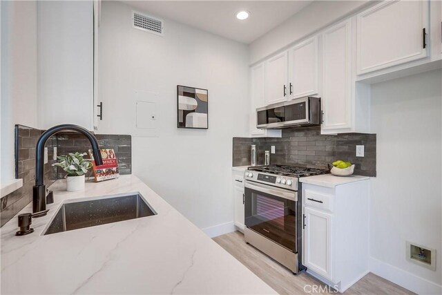 kitchen with sink, stainless steel appliances, white cabinets, and light stone countertops