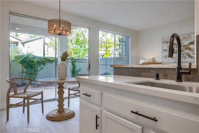 interior space featuring white cabinetry, sink, decorative light fixtures, and light hardwood / wood-style flooring