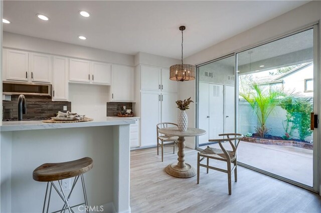 kitchen featuring decorative light fixtures, tasteful backsplash, a breakfast bar area, white cabinets, and light wood-type flooring