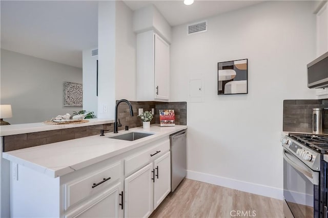 kitchen with sink, appliances with stainless steel finishes, white cabinetry, backsplash, and light wood-type flooring