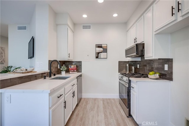 kitchen featuring sink, appliances with stainless steel finishes, white cabinetry, decorative backsplash, and light wood-type flooring