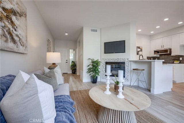 living room featuring a tile fireplace, sink, and light hardwood / wood-style flooring