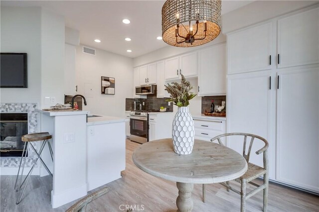 kitchen with appliances with stainless steel finishes, decorative light fixtures, tasteful backsplash, sink, and white cabinets