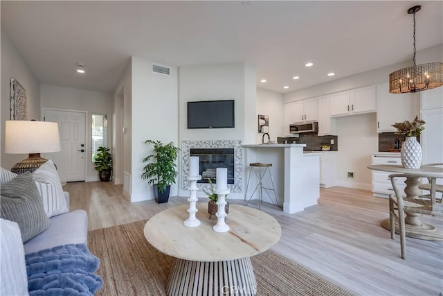 living room featuring a tiled fireplace, a chandelier, and light wood-type flooring