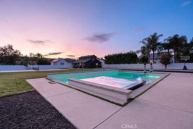 pool at dusk with a patio area and a lawn