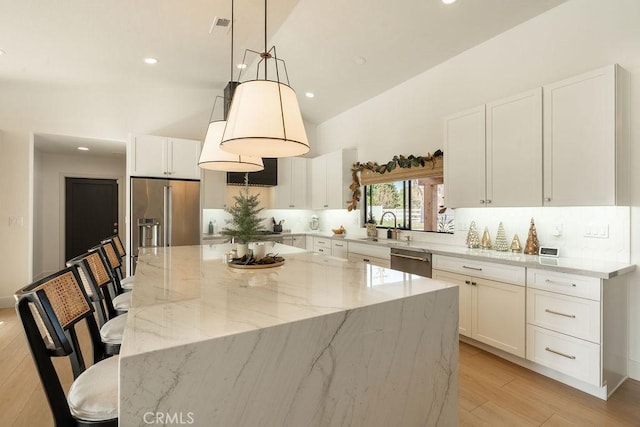 kitchen with white cabinetry, decorative light fixtures, a center island, appliances with stainless steel finishes, and light stone countertops