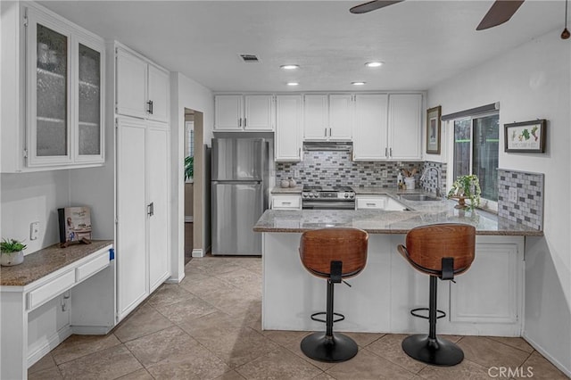 kitchen with sink, appliances with stainless steel finishes, white cabinets, a kitchen bar, and kitchen peninsula