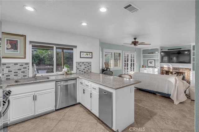 kitchen with appliances with stainless steel finishes, sink, white cabinets, light stone counters, and kitchen peninsula